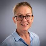 Forsker Marthe Indset i blå skjorte og med briller som ser i kamera og smiler.
