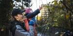 A smiling man lifting a small child up towards leaves on a tree. Photo: Benjamin A. Ward