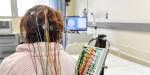 EEG electrodes attached to the back of a woman's head. Hospital environment in the background.