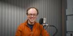 Mann sitter foran en mikrofon i studio.