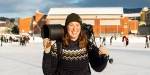 Annika smiler foran en skøytebane, og hun bærer kameraet med den store telelinsa over skuldrene.