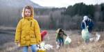 Clild in front. Blurred adults picking garbage in nature behind