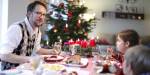Mann og to barn sitter rundt julepyntet bord. De spiser julemat, og rommet er pyntet til jul.