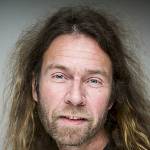 Portrettbilete av NIBR-forskar Arne Holm med langt hår og skjegg som ser i kamera og smiler.