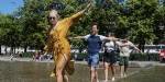 Four happy students dressed in summer outfits balancing barefoot in a fountain in central Oslo, Norway.