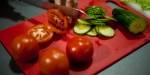 Skjærebrett med tomater som noen kutter med kniv samt agurkskiver