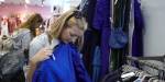 Jente prøver blått klesplagg i bruktbutikk.
