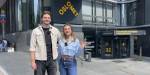 Ole og Fatima står foran OsloMet campus pilestredet og smiler. Fatima vinker til kamera