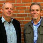 Nærbilde av Øystein Spjelkavik og Erik Lieshagen foran en rød murvegg.