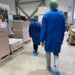 To av studentene i blå frakker og grønne hetter på besøk i emballasjefabrikken.