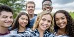 En gruppe på seks smilende unge mennesker tar selfie.