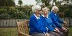 Three older women i blue jackets sitting on bench laughing