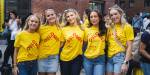 Fem jenter står på rekke på campus og smiler til kamera. De har på seg t-skjorter med OsloMetlogo og smiler til kamera. Studiestart og fadderuke.