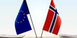 et eu-flagg og et norge-flagg står sammen på et bord med noen dokumenter ved siden av