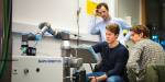 tre bachelorstudenter i automatisering og robotikk står rundt en skjerm og følger konsentrert med på hva som skjer.
