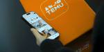 hånd holder mobiltelefon med en oransje boks med temu i bakgrunnen