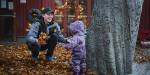 Kid playing in the leaves with an adult in kindergarten.