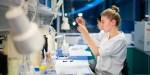 Farmasistudent på master holder opp og ser på et reagensglass i laben.