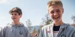 To smilende 16-åringe gutter med hettegenser ute i landlig miljø.