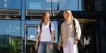 Two students walking together in front of the Kjeller campus entrance.