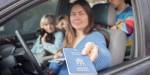 A person in the driver's seat of a car is holding out a Ukrainian passport. Two children are visible in the back seat, one of them holding a small dog. All faces are blurred.