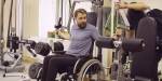 Mann med bart i rullestol trener armmuskler i et treningapparat.
