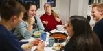 Students around a student housing kitchen table having pasta, laughing and having a good time.