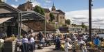 People at a restaurant sitting outside in the sun. Akershus fortress and the fjord in the background.