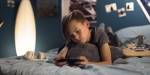 gutt som ligger på magen på senga og gamer på mobiltelefon