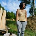 Julianne stands next to a tree stump out in the yard. On the stump is a small cup she has made of wood.