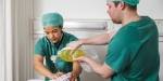 To masterstudenter i anestesisykepleie øver seg på pleieprosedyre med en treningsdukke. De har på seg grønn sykepleieuniform.