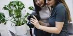 Two young women are looking at a photo on a DSLR camera.