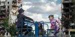 Smiling children playing on a carousel in front of shelled houses