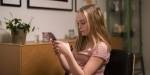 13-årig lyshåret jente i stol i stue med mobilen foran seg.