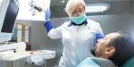 Adult male in a dentist chair looking up at female dentist in white coat.