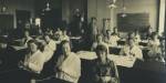 Elever ved Den kvinnelige industriskole sitter ved pultene sine og strikker.