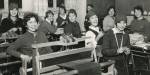 Kvinnelige studenter fra tegneklassen i 1959 sitter ved pultene sine og strikker. Alle har nisseluer.