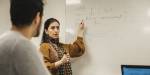 Teaching a class in Mathematical Modelling and Quantum Technologies, pointing to a whiteboard with drawings.