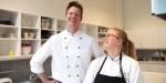 Nils Petter og Kamilla står på et industrikjøkken med kokkeuniformer. De ler og smiler sammen.