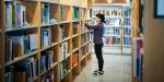 En kvinne står og sorterer i bøker på et bibliotek.