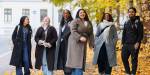 seks studenter står på fortauset og smiler til fotografen. Rundt de er det gule blader på trærne og høst.