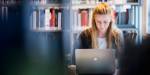 Kvinnelig student jobbar på ein laptop i eit bibliotek