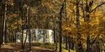 Small, round glass building blending into the autumn colours of the trees in a park.