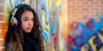 Young girl with head phones staring outwards leaning against grafitti brick wall
