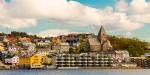 Småbyen Kristiansund i Møre og Romsdal sett frå sjøen med bustad hus og kyrkje, blå himmel og kvite skyer.