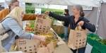 mathandel på Bondens marked, produsent gir papirposer med grønnsaker til to kunder