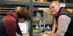Two of the students at the 3D printer, which is printing parts for the wind tunnel.