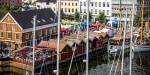 Oversiktsbilde over Arendal havn med båter, bygninger og mennesker.