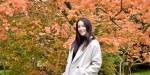 Portrait of Carla Louise Hughes. She is standing outside smiling in front of an autumn coloured tree.