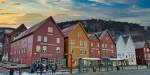 Bryggen i Bergen om vinteren med røde, oransje og hvite trehus, og folk som venter på bybanen foran husene.